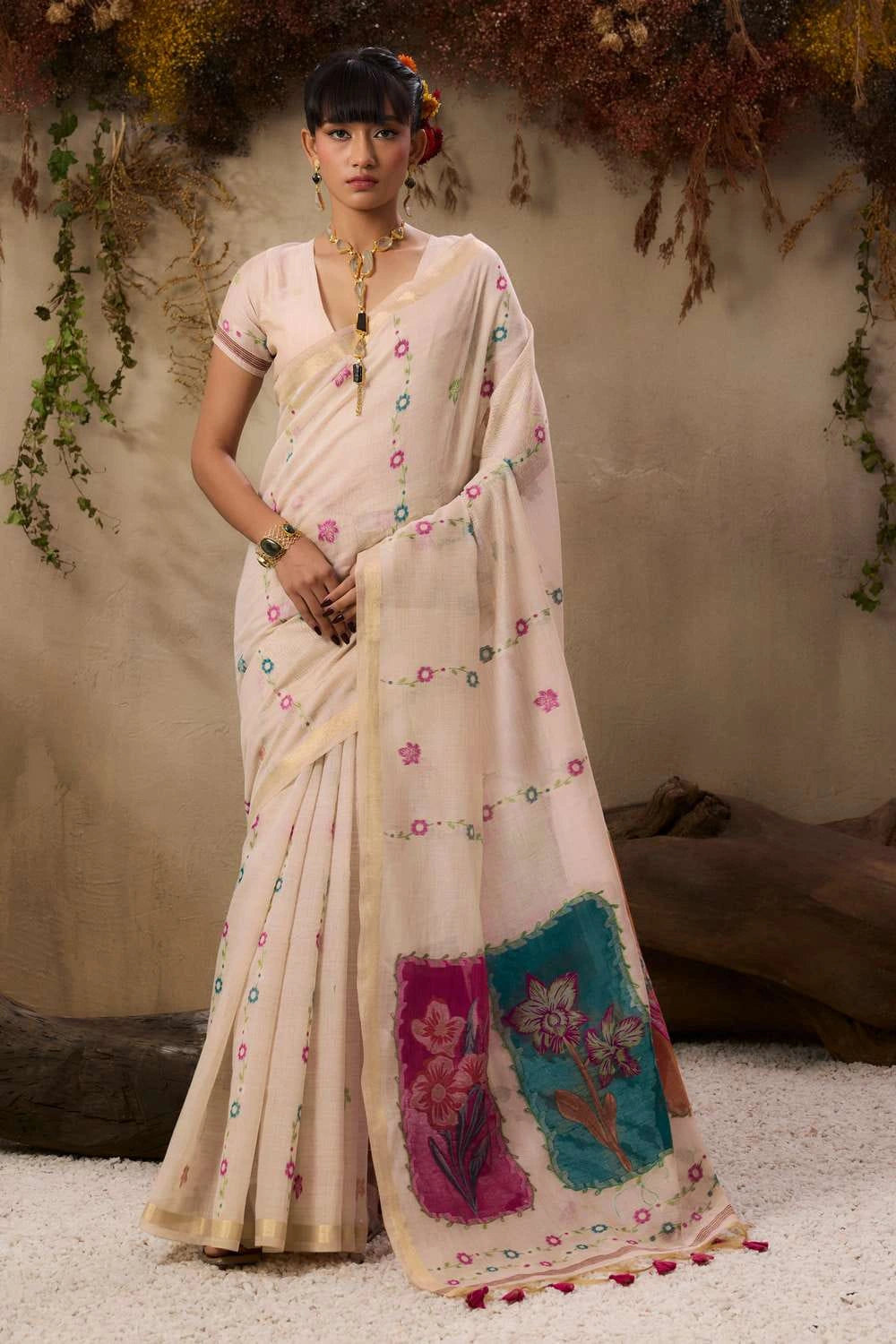 The saree has subtle pastel patterns and a bold floral accent near the pallu edge.